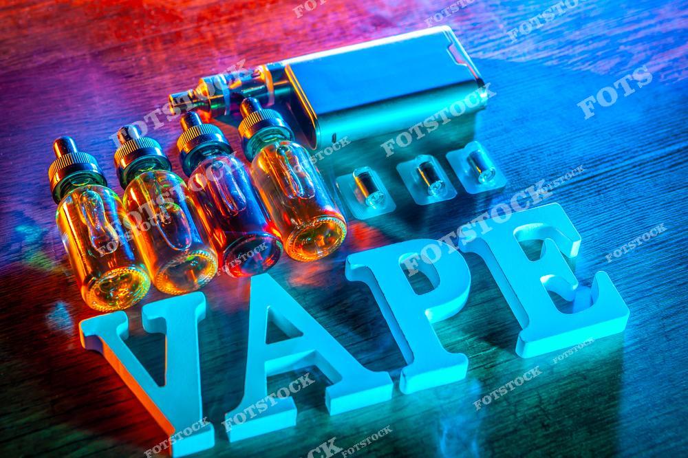 Стильное изображение с надписью VAPE, электронной сигаретой и аксессуарами для вейпинга на столе. На фотографии представлены жидкости для вейпа, современные vape-устройства и аксессуары для электронного курения, создающие атмосферу современной vape-культуры и технологичного lifestyle. Композиция идеально подходит для рекламы vape shop, интернет-магазинов электронных сигарет и товаров для вейперов. Изображение отлично подойдет для маркетинговых материалов, баннеров, публикаций о вейпинге и продвижения современных устройств для альтернативного курения.